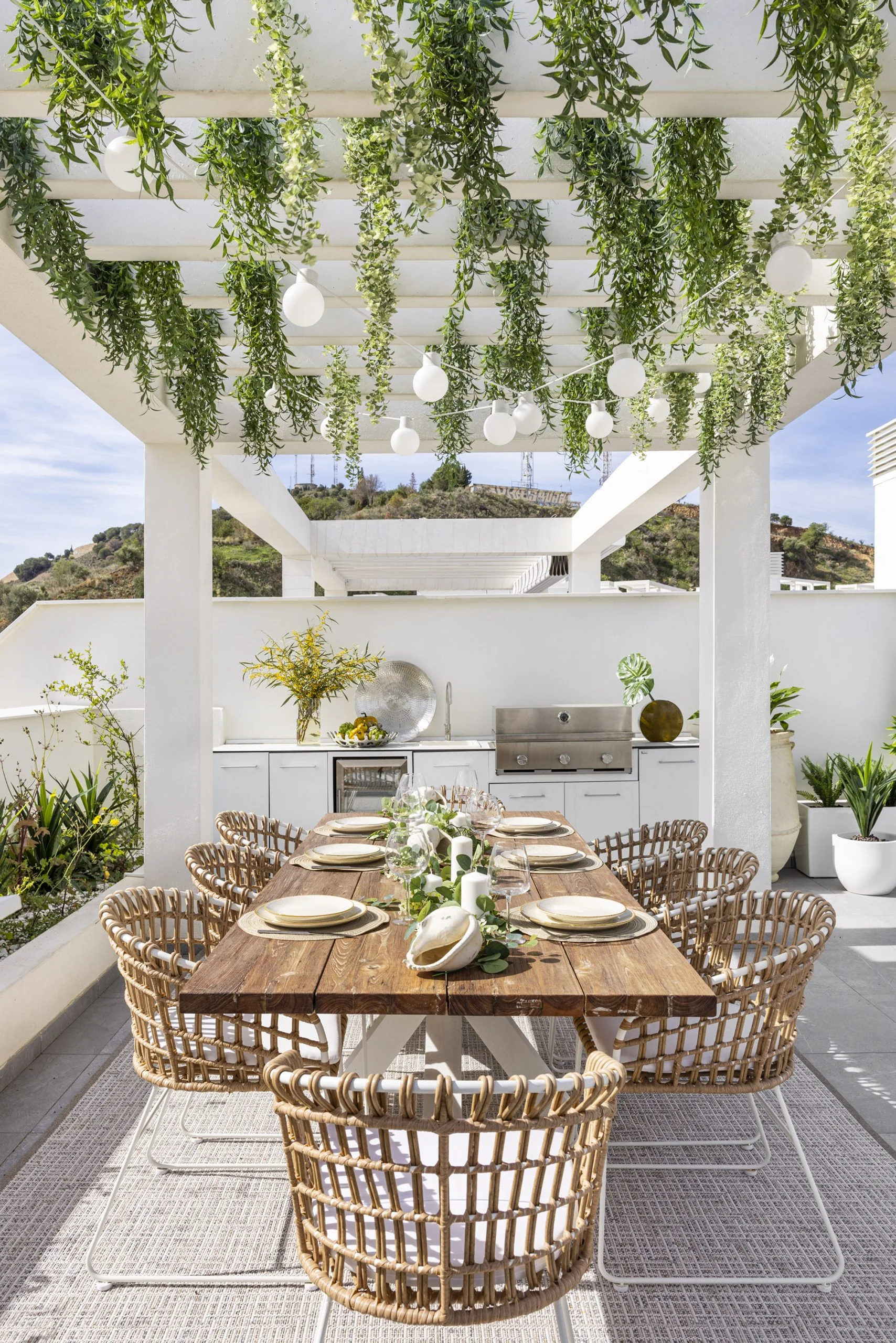 Terraza con comedor y cocina exterior bajo pérgola vegetal en un ático dúplex de El Limonar, Málaga