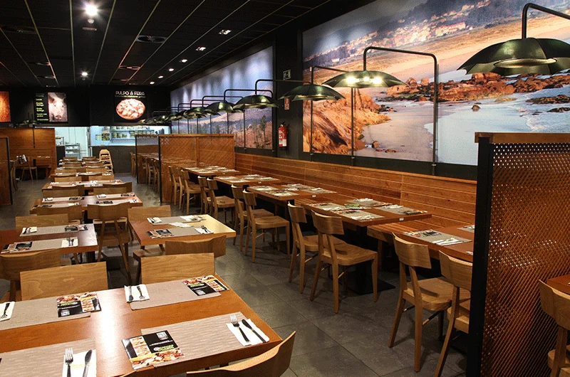 restaurante industrial con sillas y mesas de madera y lámparas -de metal decorado por PortobelloStreet